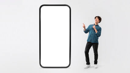 Cheerful Guy Pointing Fingers At Large Smartphone Screen, White Background