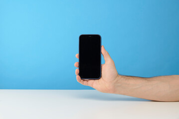 main d'un homme qui tient un smartphone sur fond bleu de studio pour publicité