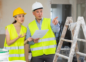 Wall Mural - Caucasian man and woman builders discussing project documentation in apartment. Pointing finger gesture.