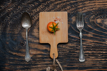 Wall Mural - one ripe cherry tomatoes on cutting board.Fork and knife on dark wooden table. view from above.