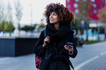 Wall Mural - young African American business woman using mobile phone in city of Latin America, Hispanic financial and caribbean people with skyscraper background on winter