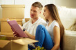 © lenets_tan - Young couple holding album while sitting on floor in new house