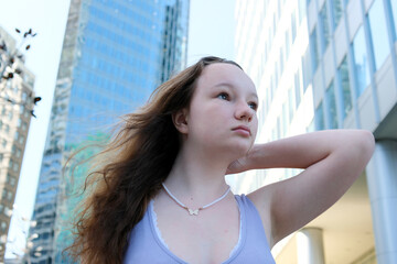 beautiful young woman in big city high skyscrapers summer t-shirt close-up face butterfly pendant around neck beads loose hair confident and look into the future go to university go to another city