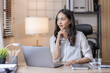 © David - Business And Education Concept. Smiling young asian woman sitting at desk working on laptop writing letter in paper documents, free copy space. Happy millennial female studying using laptop