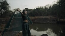 Wide Shot Of Alone Indian Girl With Traditional Dress Enjoying Cool Breeze By Holding Dupatta Near Abandoned Lake 