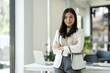 © crizzystudio - Businesswoman or office worker standing with crossed arms smiling confident working with laptop computer to record data from documents in financial folder Online , income, taxes at office desk.