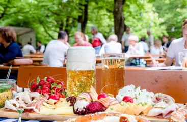 Wall Mural - Genuss im Biergarten: Maß und Brotzeitbrett mit lebhaftem Hintergrund