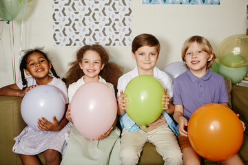 Wall Mural - Diverse group of children holding balloons and smiling at camera during party for children shot with flash