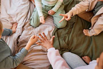 Wall Mural - Top view closeup of group of kids playing rock paper scissors while sitting on bed in circle, copy space