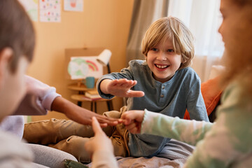 Wall Mural - Group of children playing rock paper scissors while sitting on bed in circle, copy space