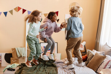 Wall Mural - Full length view at diverse group of little children jumping on bed together and having fun