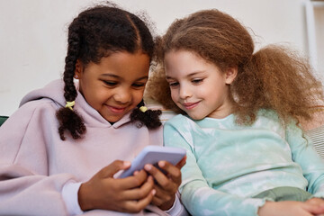 Wall Mural - Portrait of two cute little girls using smartphone together and playing mobile games