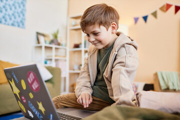 Wall Mural - Side view portrait of smiling boy looking at computer screen while using internet at home