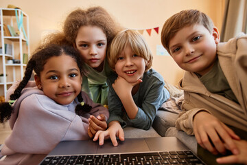 Wall Mural - POV Group of children looking at computer screen together huddled over laptop and smiling