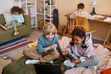 Wall Mural - Portrait of two kids playing videogame on bed with laptop, copy space
