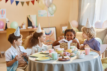 Wall Mural - Diverse group of happy kids at Birthday party with little girl opening presents
