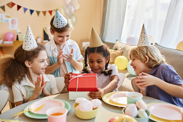 Wall Mural - Diverse group of happy children at Birthday party with little black girl opening presents