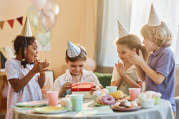 Wall Mural - Diverse group of happy children at Birthday party with little boy opening presents