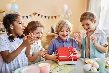 Wall Mural - Diverse group of happy children at Birthday party with excited boy opening presents