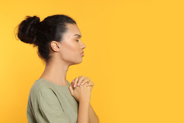 African American woman with clasped hands praying to God on orange background. Space for text