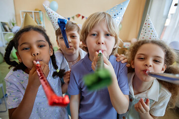 Wall Mural - Front view portrait of three children holding party blowers and having fun at Birthday celebration