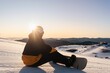 © Frankie Swof_ph/Wirestock Creators - Snowboarder sitting on the snowy ground at sunset