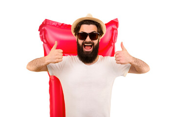 studio portrait of a bearded man in sunglasses and a panama hat, the guy is  showing likes, standing on background a pink inflatable swimming mattress, concept of vacation at sea and summer mood