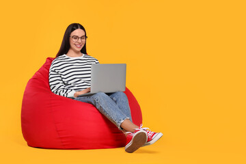 Poster - Happy woman with laptop sitting on beanbag chair against orange background