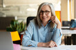 © Maria Vitkovska - Portrait of smiling confident senior businesswoman, real estate agent, looking at camera in modern office. Gray haired manager wearing stylish eyeglasses sitting at workplace. Successful business