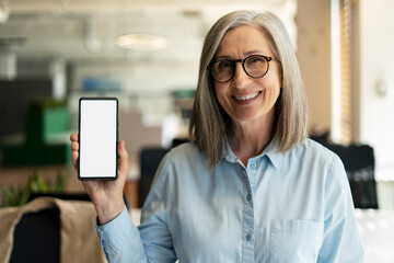 Portrait of attractive smiling senior woman holding mobile phone, showing digital screen, mock up. Happy 60 years old, gray haired  female using modern mobile app shopping online. Technology concept