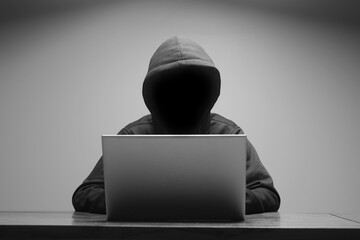  Mysterious man wearing black hoodie using laptop in the dark room. Hacker and cyber security concept.