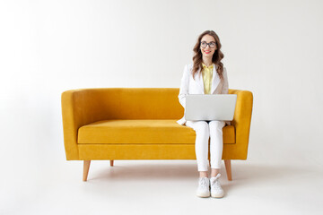 young businesswoman in suit sits on comfortable soft sofa and uses laptop, girl in formal wear is typing on computer