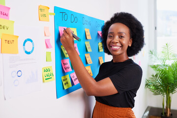 Black woman scrummaster writes on KANBAN board with ticket backlog, sprint plan