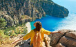 Traveler girl on vacation sitting on cliff, freedom opening arms, enjoying amazing panoramic view of Butterfly Valley Beach