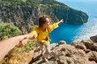 Happy tourist woman holding her boyfriend hand, showing him towards the breathtaking scenery of Butterfly Valley Beach. Couple exploring scenic landscape with crystal clear turquoise water
