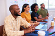 © Meeko Media - Four diverse team members sit in a row in a meeting, listening to presentation