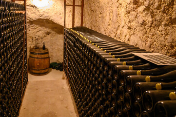 Wall Mural - Walking in deep undergrounds caves with bottles on wooden racks, making champagne sparkling wine from chardonnay and pinor noir grapes in Epernay, Champagne, France