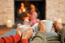 Hands, Coffee And Couple Relax By Fireplace, Bonding And Cozy In Home Together. Tea, Man And Woman Relaxing By Fire On Christmas Holiday In Winter, Heat And Enjoying Quality Time With Drinks In House