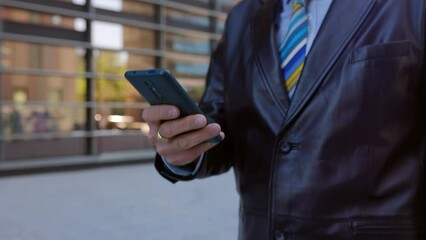 Close up view of businessman using smartphone while walking on city street. Texting online message, scrolling and touching mobile phone screen while scrolling social media content on app.