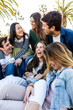 © Xavier Lorenzo - Vertical photo of happy group of millennial friends having fun sitting outdoors. Diverse college students smile and laugh together relaxing together at street. Friendship and youth lifestyle concept.