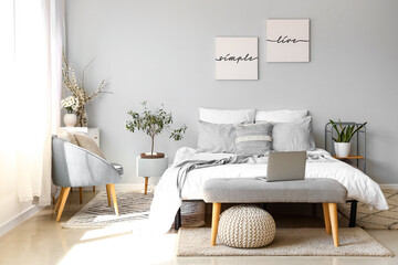 Poster - Interior of light bedroom with modern laptop on bedside bench and blooming tree branches