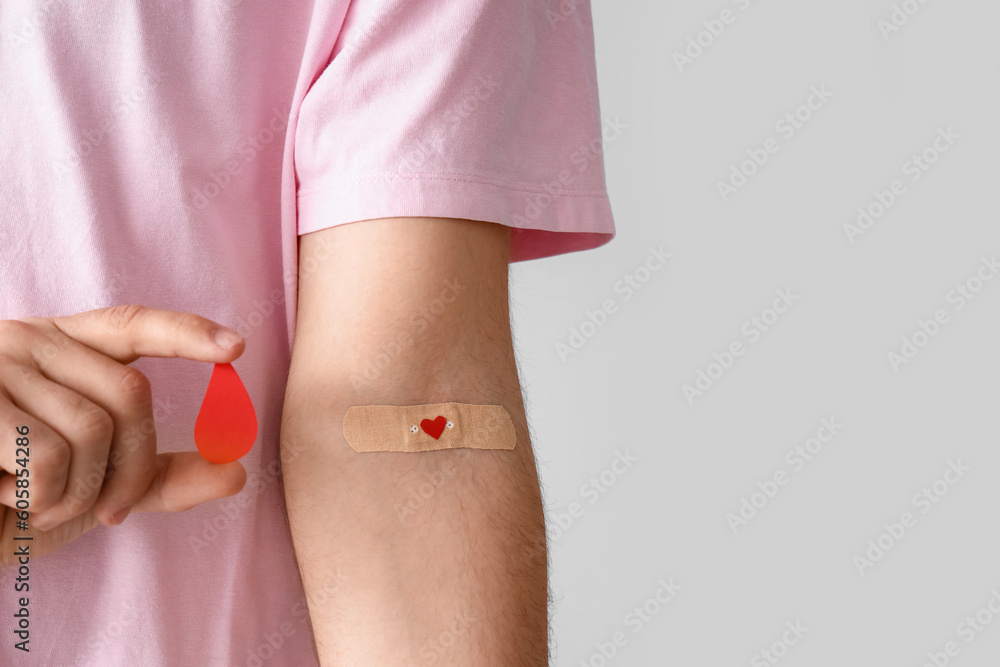 Young blood donor with applied medical patch and paper drop on light background, closeup