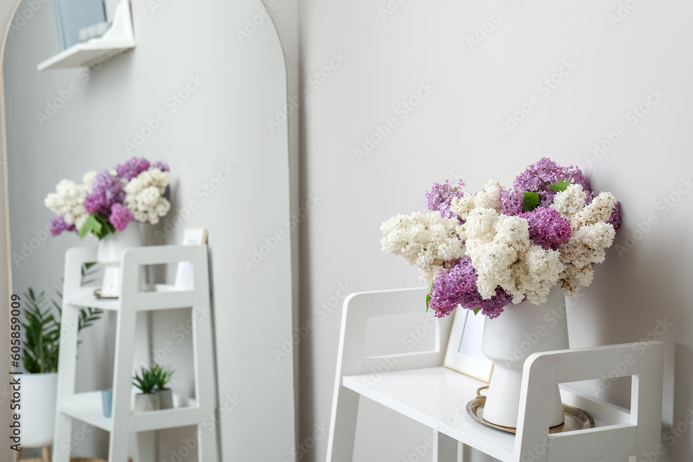 Vase with lilac flowers and frame on shelf in light room