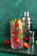 Wall Mural - Glass of fresh strawberry mojito with shaker and jigger on grunge green background