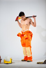 Wall Mural - Topless professional firefighter with a sweaty body is standing on a white background holding an iron axe on his shoulder while looking at the floor.