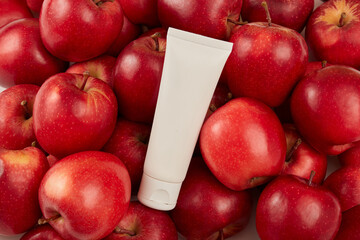Wall Mural - Against a ripe red apples background, an empty plastic tube unbranded are placed. Mockup for cosmetic, cream or cleanser from apple ingredient. Cosmetics product and promotion concept for advertising