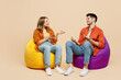 © ViDi Studio - Full body smiling young couple two friends family man woman wear casual clothes together sit in bag chair talk speak spread hands isolated on pastel plain light beige color background studio portrait.