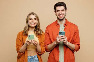 Canvas Print - Young smiling happy cheerful couple two friends family man woman wear casual clothes hold in hand use mobile cell phone together isolated on pastel plain light beige color background studio portrait.