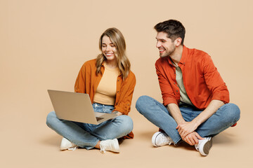 Full body young couple two friends family IT man woman wear casual clothes together sitting hold use work on laptop pc computer isolated on pastel plain light beige color background studio portrait.