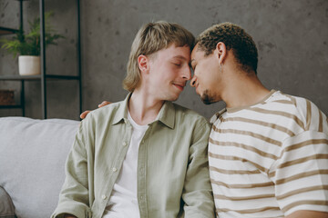 Wall Mural - Young happy couple two gay men wear casual clothes together touch forehead close eyes sit on sofa couch at home flat rest spend free spare time in living room. Pride day june month love lgbtq concept.